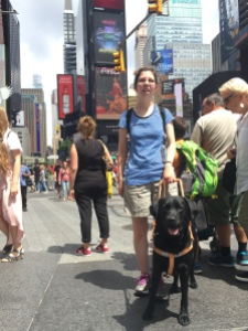 Jameyanne standing in front of a crowd in Time Square with Neutron at her side. Both person and puppy are smiling.